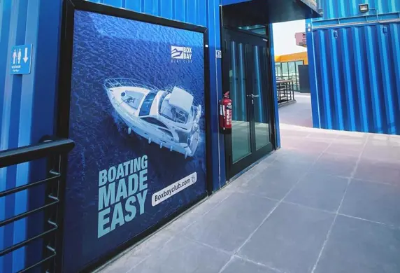 A large smart blue container with glass double doors and a sign on the outside "Boating Made Easy" boxbayboatclub.com