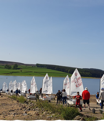 A group of people taking their rigged Oppie dinghies from the club to the water at Derwent Reservoir Sailing Club, Consett, County Durham
