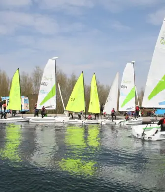 A group of Picos with different coloured sails sailing on calm water