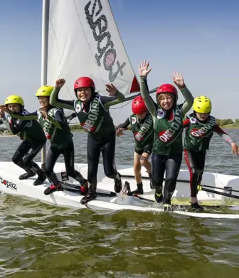 A group of children at a kids camp standing on a small sail boat about to jump into the water