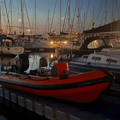 A marina at late sunset with an orange rigid inflatable boat (RIB) just visible at the front