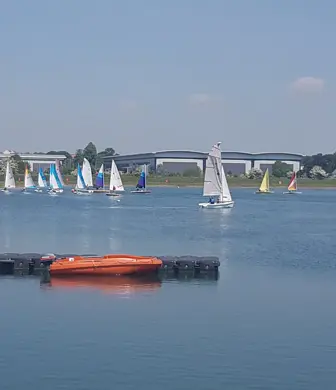 A group of dinghies sailing on Grimsby Reservoir with an orange rigid inflatable boat (RIB) in the foreground at Banbury Cross Sailing Club