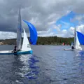Two sailing dinghies with white mainsails and jibs and bright blue spinnakers sailing on the water on a cloudy day