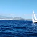 A yacht sailing alone on the open sea with the hills on the shore in the very distant background