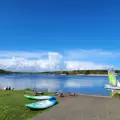 View across a lake showing dinghies on the water and paddleboards on the shore