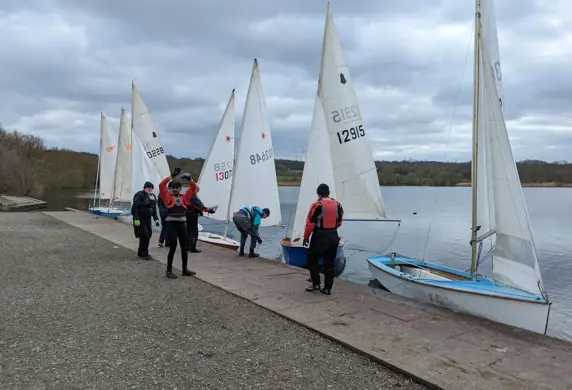 A group of people on the jetty preparing to sail their rigged dinghies on a cloudy day