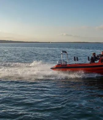 Two people on a rigid inflatable boat (RIB) speeding across the water from Rockley Point Sailing Centre, Poole, Dorset