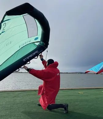 Two men practising holding their wing foils on the shore at Queen Mary Sailing Club, Ashford