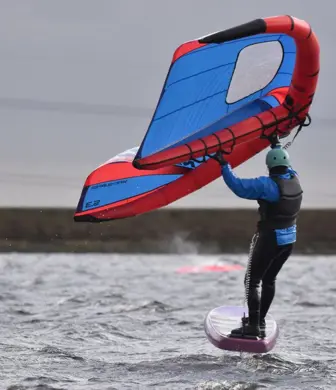 A wing foiler with a red and blue wing foil on the water at Watergrove Windsurfing Club, Watergrove Reservoir, Rochdale