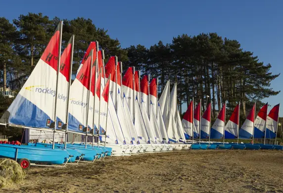 A long line of Hartley training boats with their identical red, white and blue sails up on the shore at Rockley Point Sailing Centre, Poole, Dorset