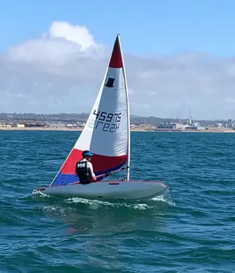A dinghy with a red and white sail heeling while the person hikes out the opposite side