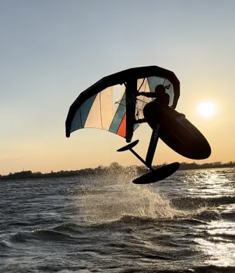 A person performing a jump whilst wing foiling on the water at the Andrew Simpson Watersports Centre, Portsmouth