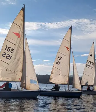 Three Laser dinghies sailing alongside each other against a blue sky with a few clouds in the sky