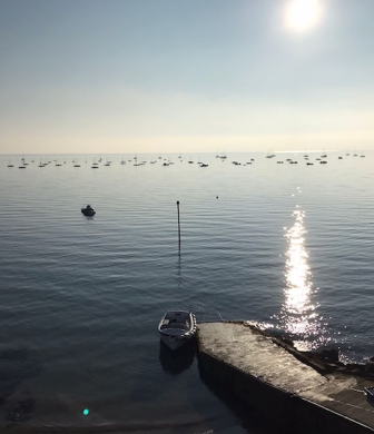 View from the jetty at South Caernarvonshire Yacht Club, Abersoch, Wales with the sun glinting off the water and mooring buoys in the distance
