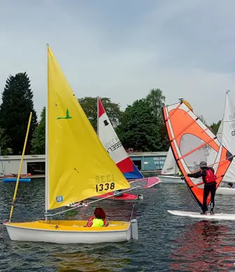 A range of watersports being displayed by Midland Sailing Club, Birmingham including a person kayaking, a sailor in a keelboat, a windsurfer and a dinghy sailor