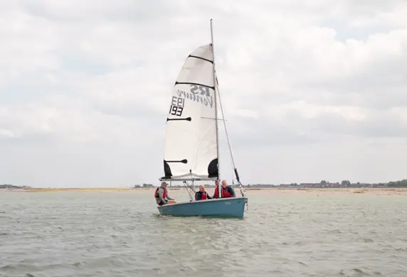 Three people on a small sail boat on the water on a calm but cloudy day at the Andrew Simpson Watersports Centre, Portsmouth