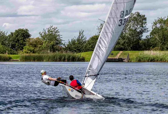 Two people sailing a Laser sail boat with one hiking out the side to help steer it