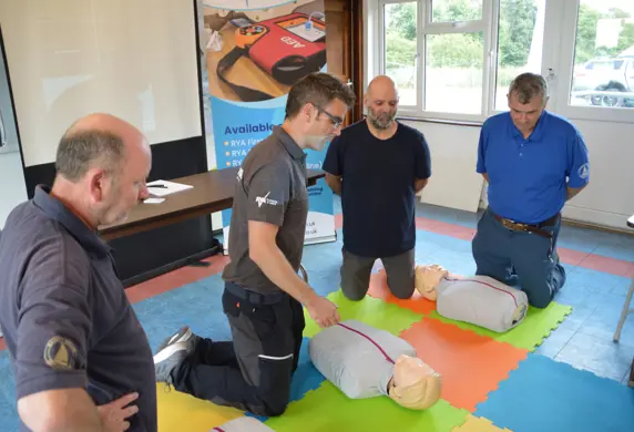 A classroom with three students and an instructor all kneeling on the floor practising resuscitation techniques during a first aid course at North Oxford Marine Training, Grimsby Reservoir, Banbury