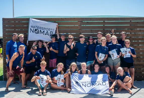 A team photo of all the people at Watersports Nomad, Vassiliki, Greece - two people are holding flags whilst several others are holding up certificates for all the courses they offer