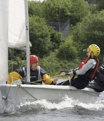 Three men sailing a Laser with one in the boat and two sitting on the edge hiking out