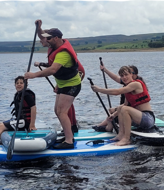 A group of five people enjoying messing about on their stand up paddle boards on the water at Derwent Reservoir Sailing Club, Consett, County Durham