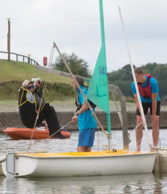 A disabled man being hoisted into a sailing dinghy to enable him to sail on the reservoir at Llandegfedd Watersports, Pontypool, Gwent