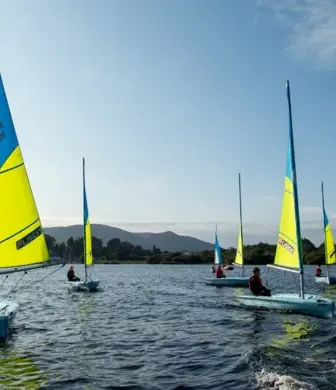 A group of Pico dinghies sailing with blue and yellow sails on Derwent Water in the Lake District
