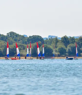 Eight Pico dinghies with identical red, white and blue sails, sailing with a safety boat from Rockley Point Sailing Centre, Poole, Dorset