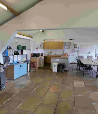 An interior of a club house with the tables pushed to once side and a barbeque and wash up area