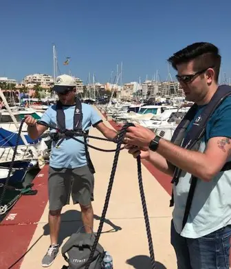 Two men on a jetty on a sunny day practising their knots