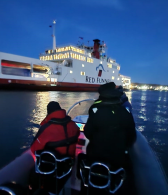 Two people on a rigid inflatable boat (RIB) at night alongside the Red Funnel Southampton-Isle of Wight car ferry at Ocean Sports Tuition, Southampton 
