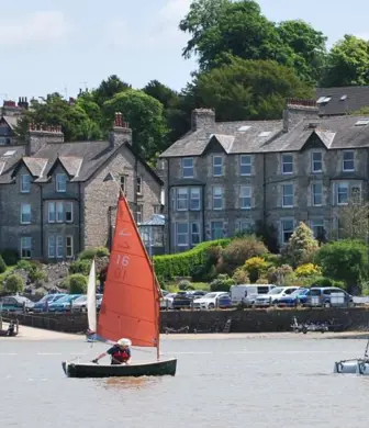 A Siren and catamaran sailing on the water with a row of terraced houses in the background