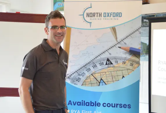 A man stood in front of a poster promoting North Oxford Marine Training available courses