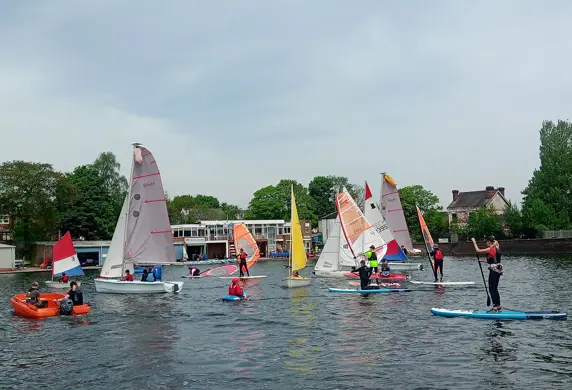 A variety of water sports taking place at Midland Sailing Club, Birmingham including paddle boarding, sailing supported by a safety boat with the club house in the background