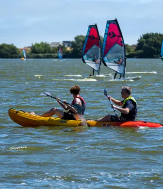 Two kayakers and three windsurfers enjoying the open water