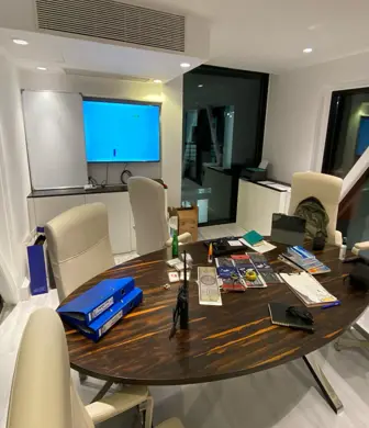 A large round wooden table with cream leather chairs around it with a large TV monitor on the wall.  The table has folders and paperwork on it at Boxbay Boat Club, Old Doha Port, State of Qatar