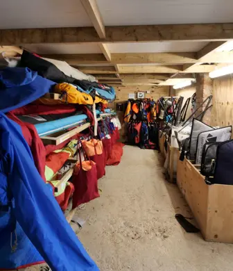 A wooden equipment store with sails in racks on the left and equipment in bags on the right