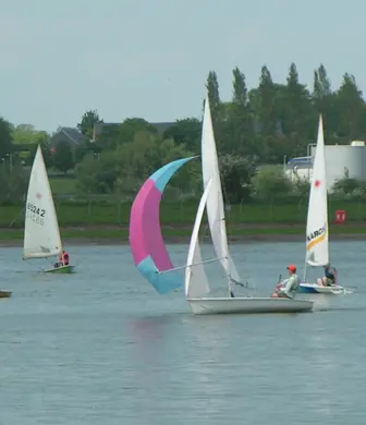 Three dinghies and a sail boat with its spinnaker up sailing on the Grimsbury Reservoir at Banbury Cross Sailing Club