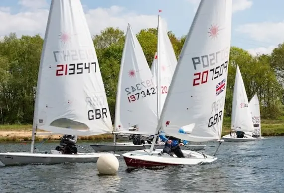 A group of Laser dinghies racing on the water with trees and the shore in the background