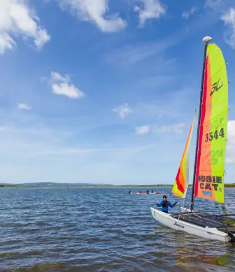 A Hobbie Cat catamaran on the water with an orange and yellow at Rockley Point Sailing Centre, Poole, Dorset