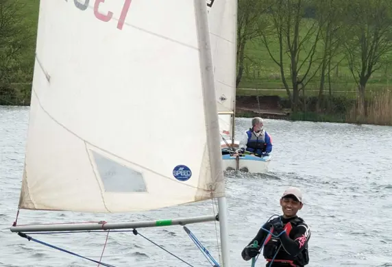 A Laser dinghy with a green hull sailing towards the camera with another dinghy following in the distance