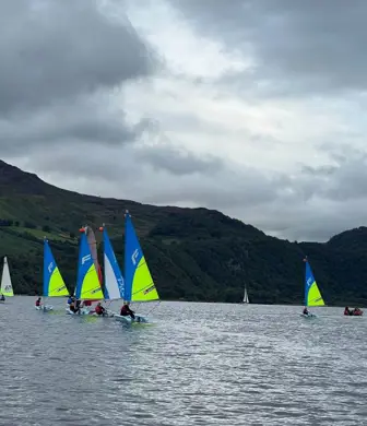 A group of Pico dinghies with blue and yellow sails sailing on Derwent Water in the Lake District