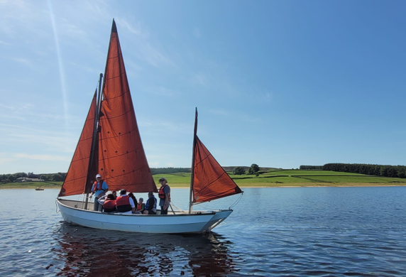 A Muriel classic sail boat with three red sails on the water at Derwent Reservoir Sailing Club, Consett, County Durham
