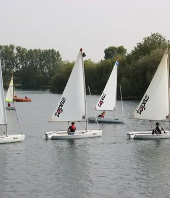 A group of young people sailing Topaz dinghies on the water with a rigid inflatable boat (RIB) in support