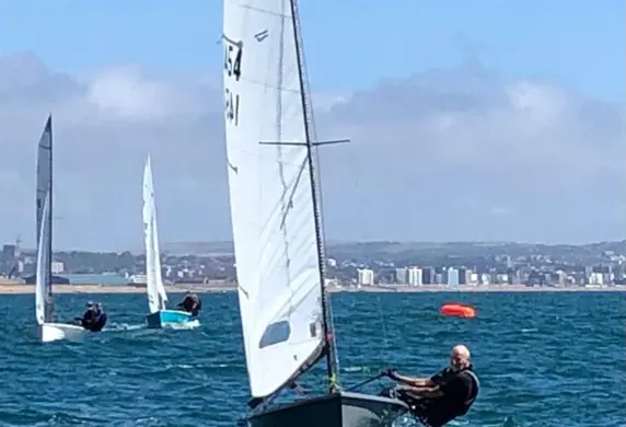 Three dinghies sailing on the water on a sunny day with the shoreline in the distance