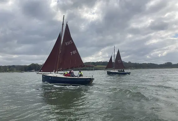 A traditional small sailing boat with two red sails on the reservoir at the Royal Hospital School Sailing Academy, Ipswich