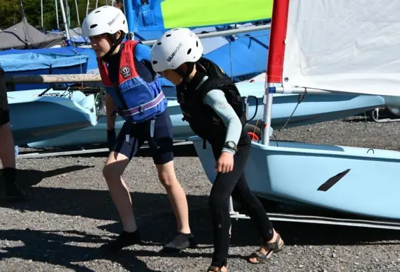 Two young poeple pulling a dinghy up the shore on a trolley