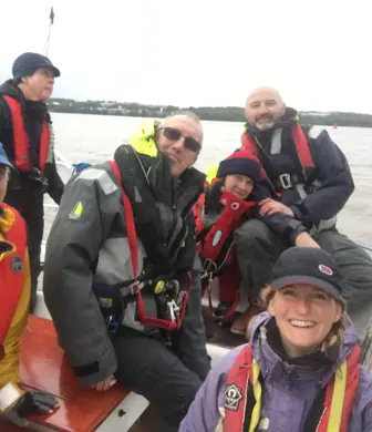 Group of women on a sailboat, smiling and wearing life jackets, enjoying a team day sailing on the water