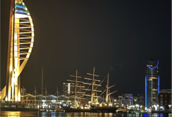 Spinnaker illuminated at night with a tall ship alongside