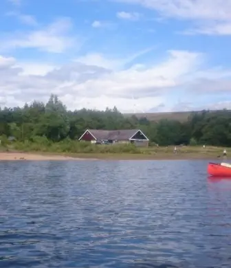 A person in a rowing boat in front of the club house at Watergrove Windsurfing Club, Watergrove Reservoir, Rochdale